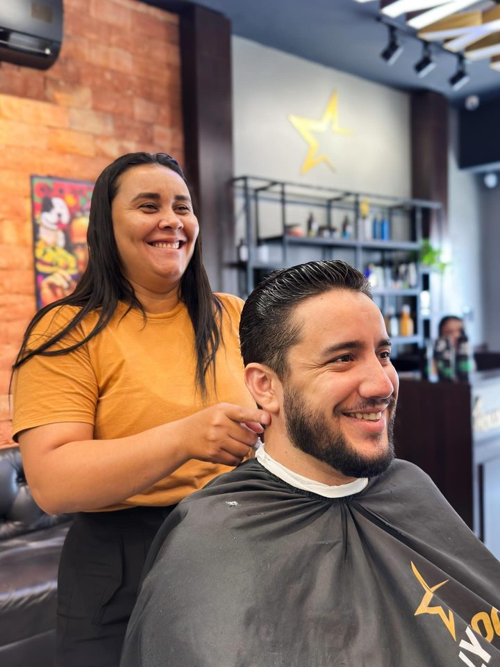 Barbeira sorrindo enquanto finaliza o corte de um cliente
